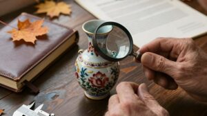 Эксперт изучает старинную вазу с лупой, проводя оценку антиквариата для страхования коллекции